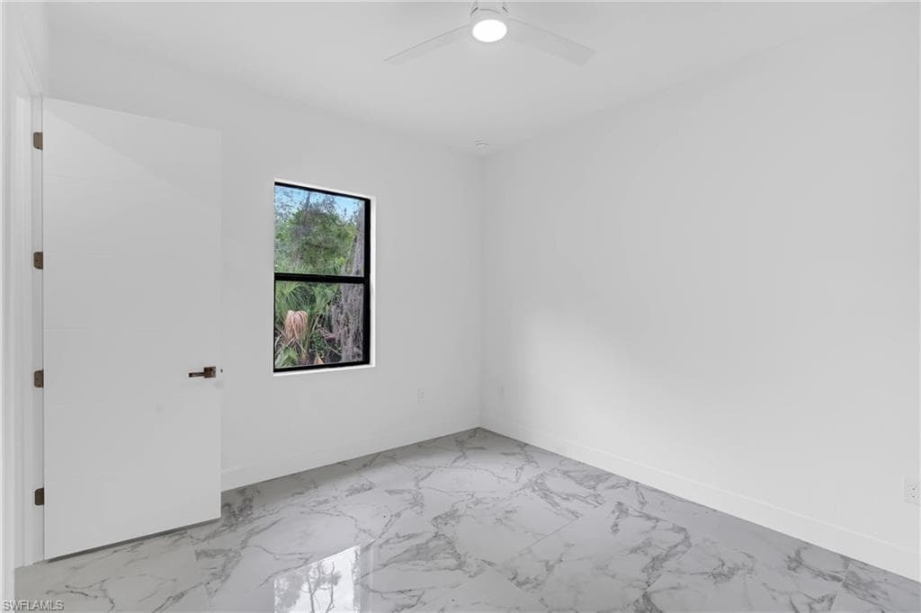 Spacious room featuring large format tile flooring, a contemporary ceiling fan with integrated lighting, a substantial window with dark trim, clean white walls, and a solid interior door with dark hardware