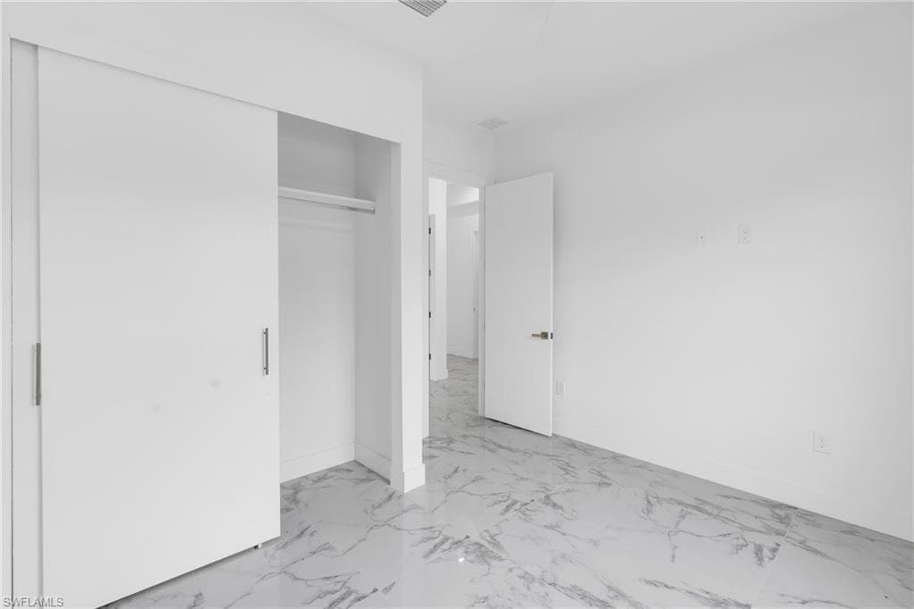 Spacious room with white walls, sliding closet doors with brushed metal pulls, and white-veined stone-finish flooring