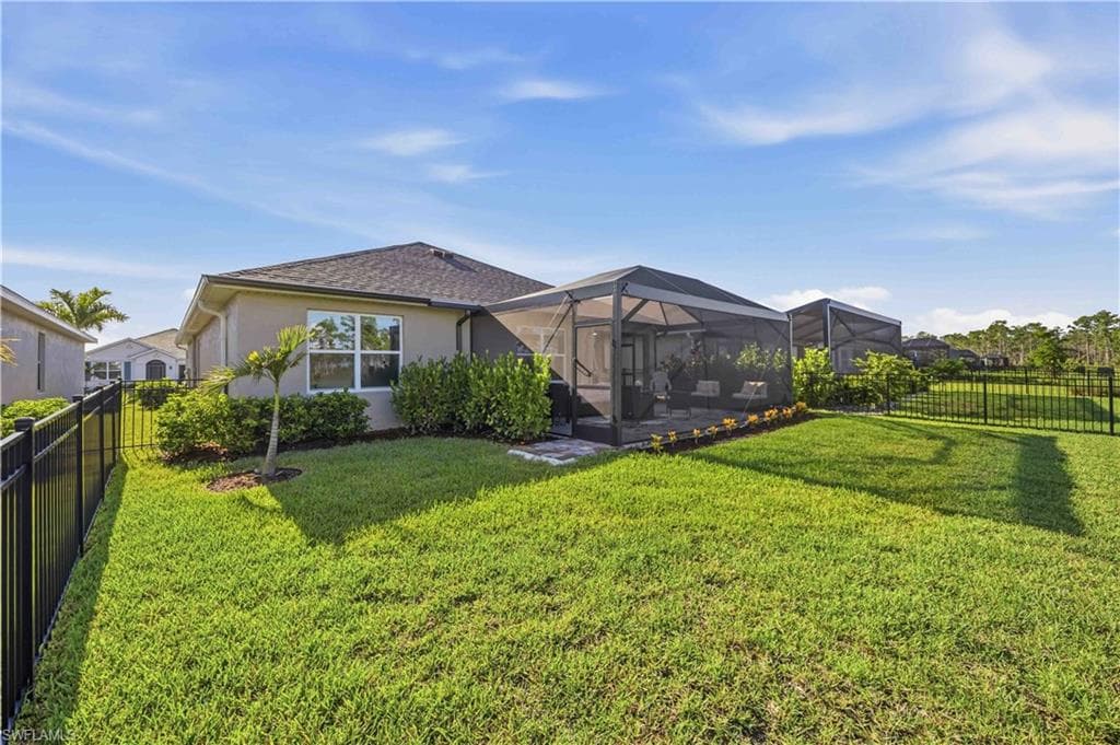Expansive backyard featuring a large screened-in lanai, manicured lawn, and black aluminum fencing