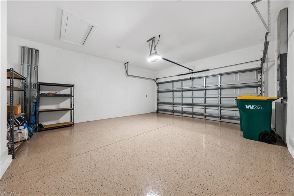 Spacious garage featuring a durable speckled epoxy floor, overhead lighting, an automatic garage door, and a ceiling-mounted access panel