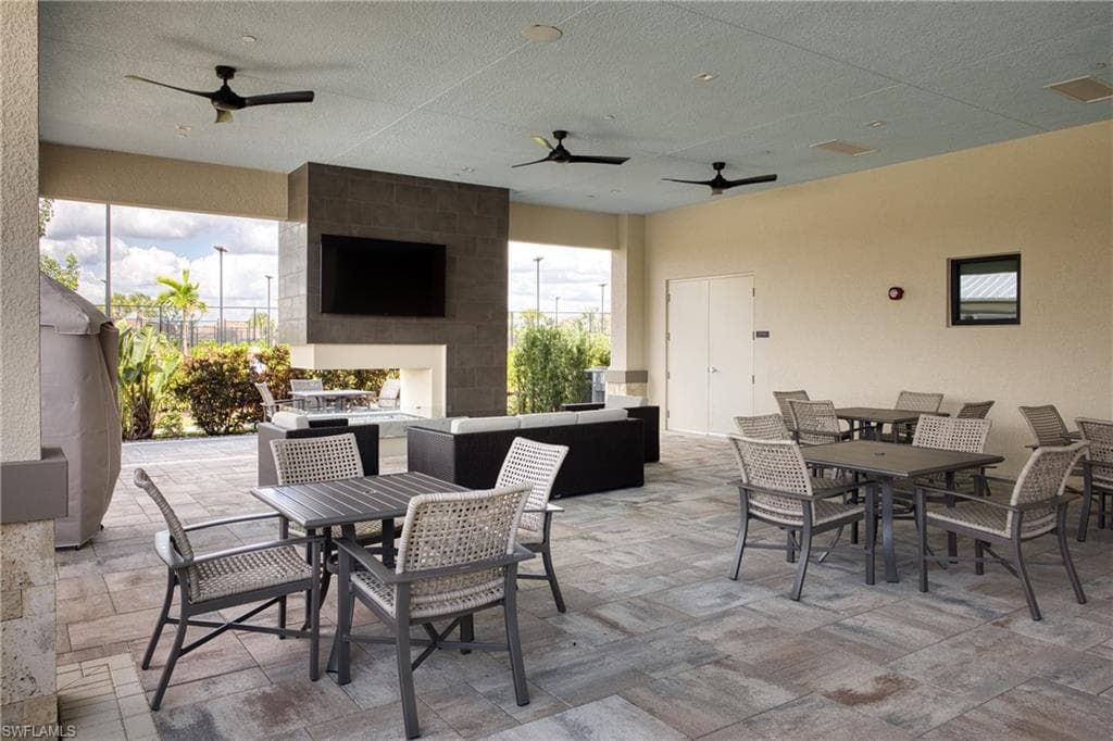 Expansive covered patio featuring patterned paver flooring, a stone-clad media wall with integrated television, and multiple ceiling fans