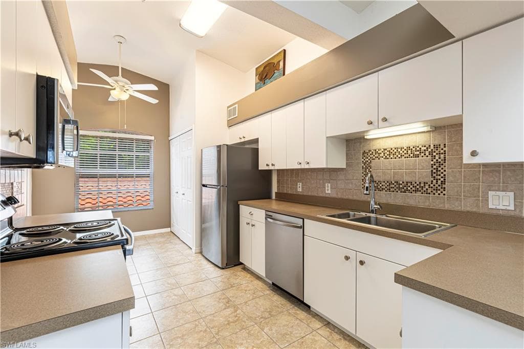 Kitchen featuring white cabinetry, light-toned countertops, stainless steel appliances, tile flooring, and a tiled backsplash with decorative inlay