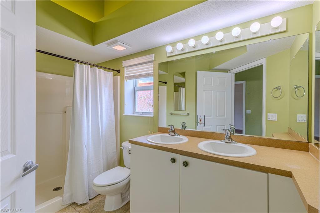 Primary Bathroom featuring a dual vanity with light-toned countertops and undermount sinks, a large wall-mounted mirror, and overhead strip lighting