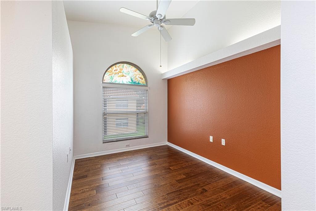 Den with vaulted ceiling wood flooring, a ceiling fan, and an arched window with blinds