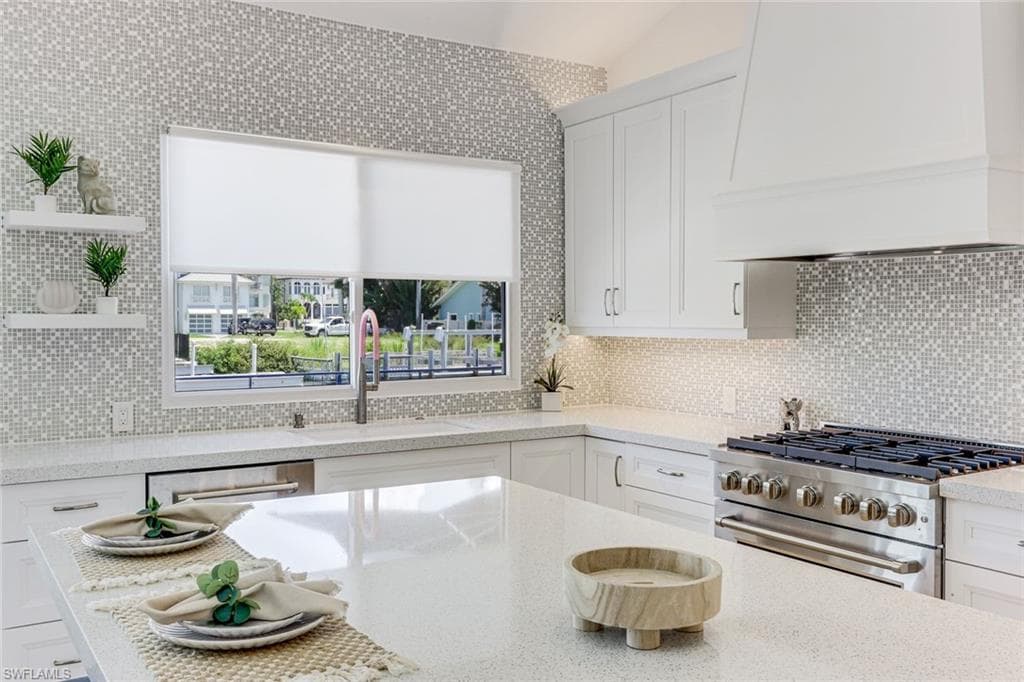 Spacious kitchen featuring white shaker cabinetry, an integrated range hood, a stainless steel gas range, and light-toned mosaic tile backsplash