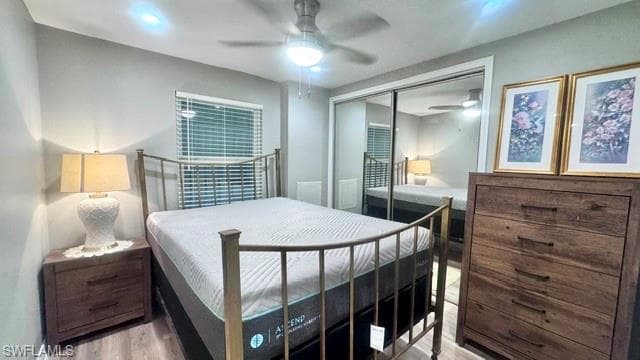 Room featuring wood-finish flooring, a ceiling fan with integrated lighting, a window with horizontal blinds, and a mirrored closet