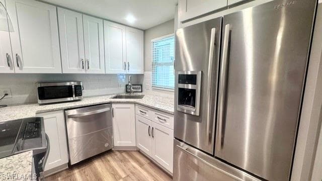 Kitchen featuring white shaker cabinetry, stainless steel appliances, speckled countertops, a white subway tile backsplash, and wood-finish flooring