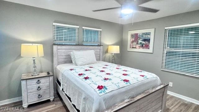 Bedroom featuring grey walls, twin windows with blinds, wood-finish flooring, and a ceiling fan