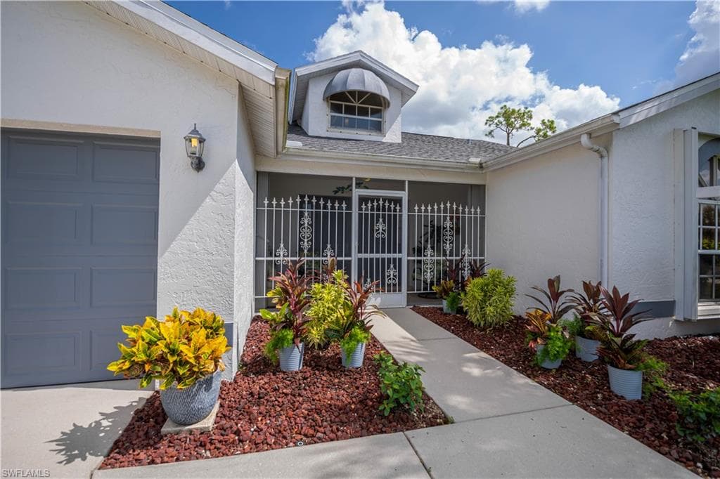 Front exterior featuring a screened entry, attached garage with a panel door, arched dormer window, concrete walkway, and decorative landscaping