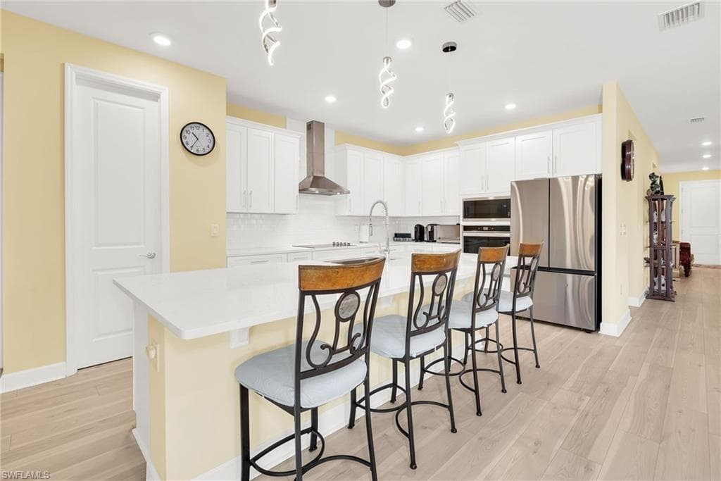 Kitchen featuring an expansive island with a white countertop, white shaker cabinetry, stainless steel appliances, a white subway tile backsplash, and light wood-finish flooring