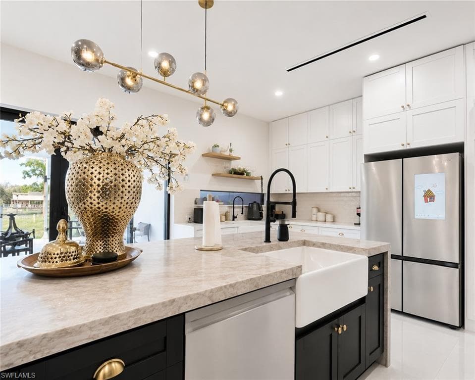 Gourmet kitchen featuring a large island with an apron-front sink, stone countertops, black cabinetry, and a modern chandelier