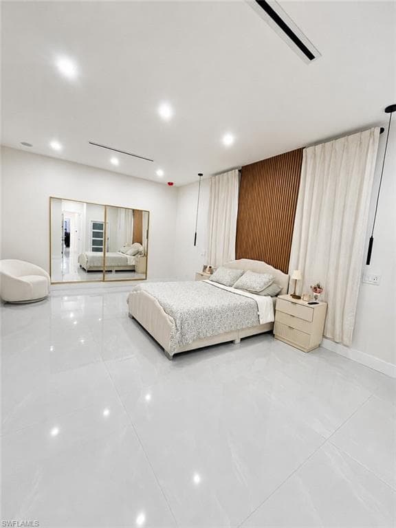 Spacious room featuring light-toned large format tile flooring, a slatted wood accent wall, recessed lighting, and full-wall mirrored closet doors with gold-toned framing
