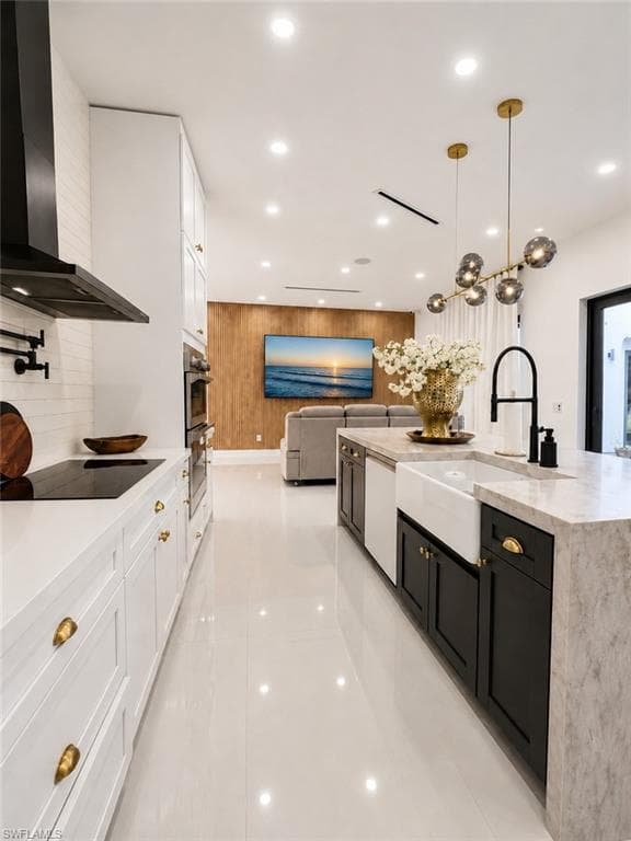Contemporary kitchen featuring white cabinetry with gold-toned hardware, a built-in cooktop, and a black range hood