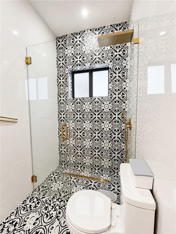 Shower enclosure featuring patterned black and white tile, gold-finish fixtures, and a glass door