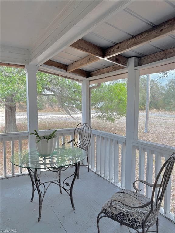 Screened porch featuring a painted wood floor, white railing, and exposed wood beam ceiling