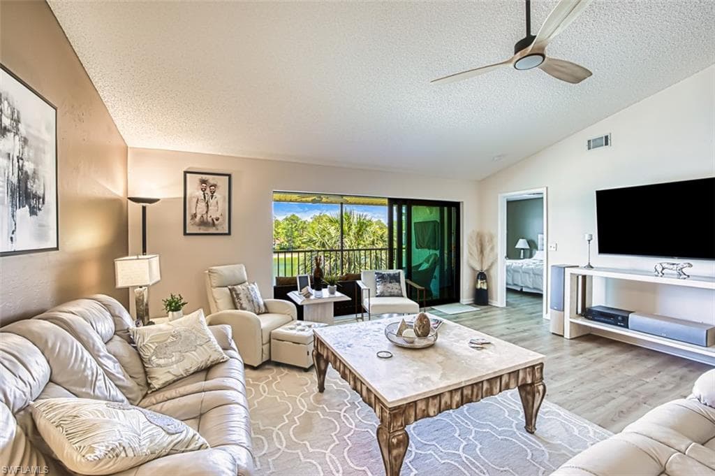 Living area featuring a textured ceiling, vaulted ceiling, ceiling fan, and light wood finished floors