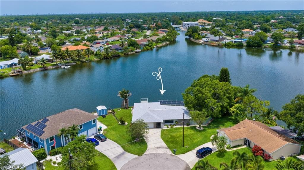 Waterfront property featuring a single-story residence with a white roof, mature landscaping, and a concrete driveway