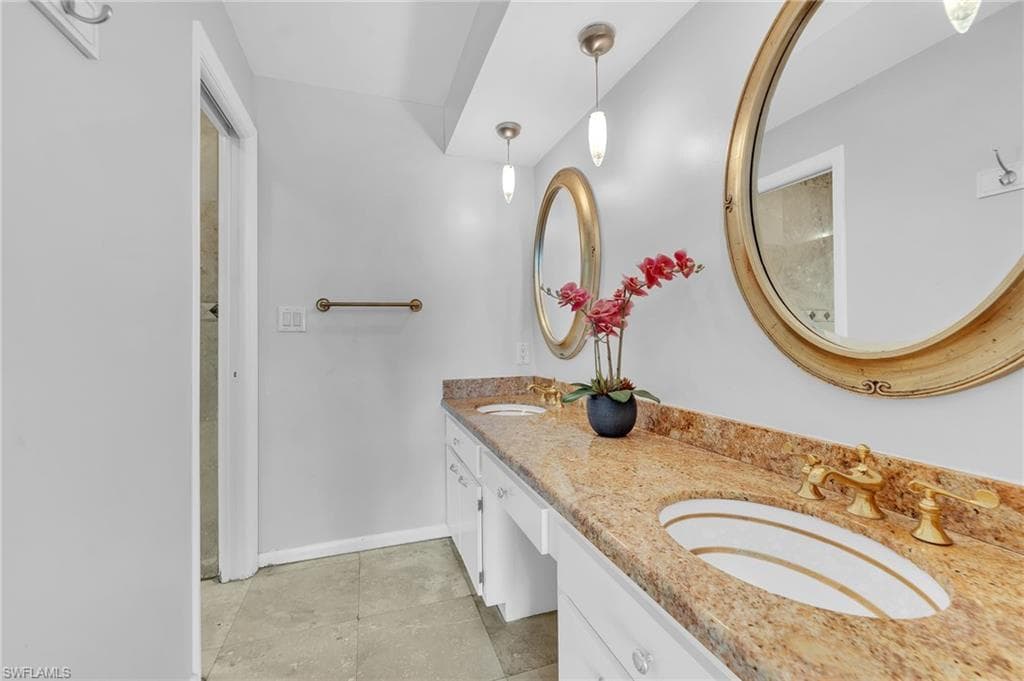 Double vanity with granite countertop, integrated sinks, brass-finish fixtures, and oval mirrors