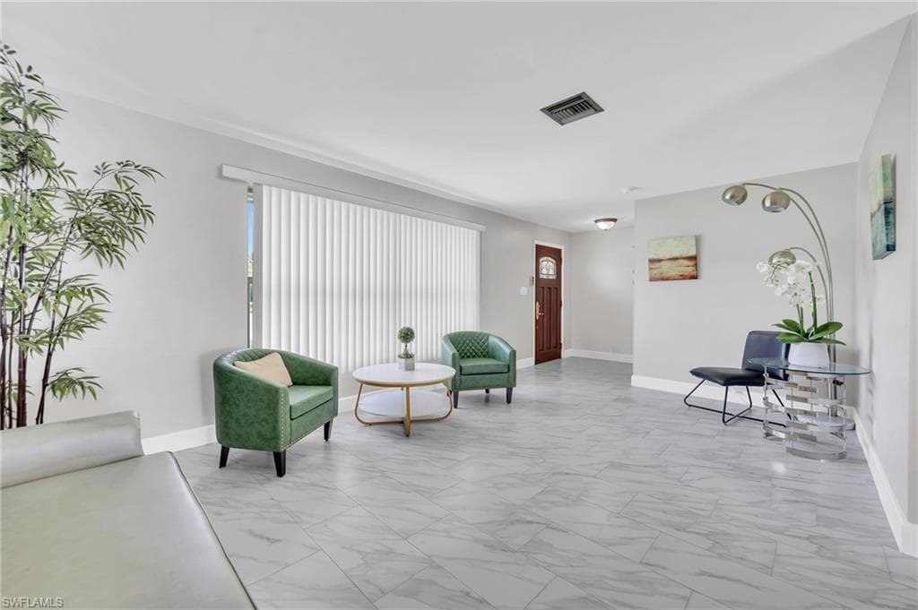Spacious living area featuring large format tile flooring, crown molding, and a wide window with vertical blinds