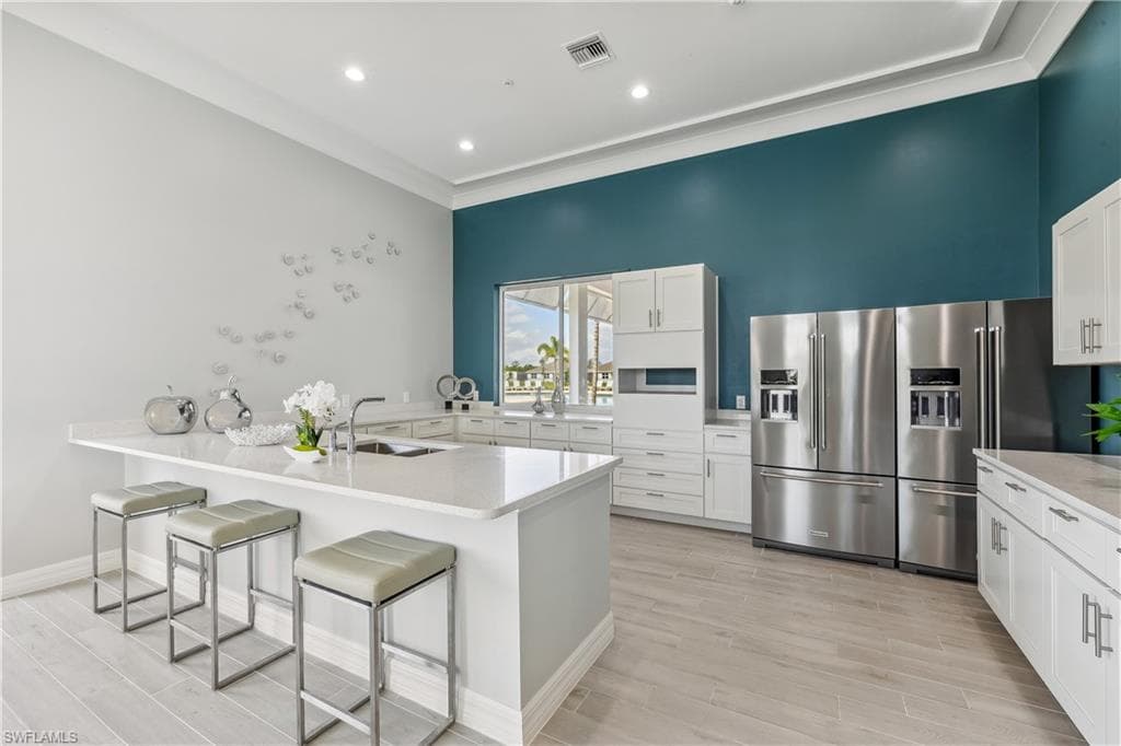 The kitchen features an expansive island with a sink, white cabinetry, stainless steel appliances, and light-toned flooring
