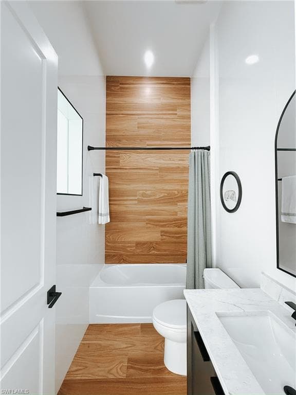 Bathroom featuring a tub/shower combination with wood-finish wall paneling, wood-finish flooring, a white vanity with a rectangular basin, and a wall-mounted mirror