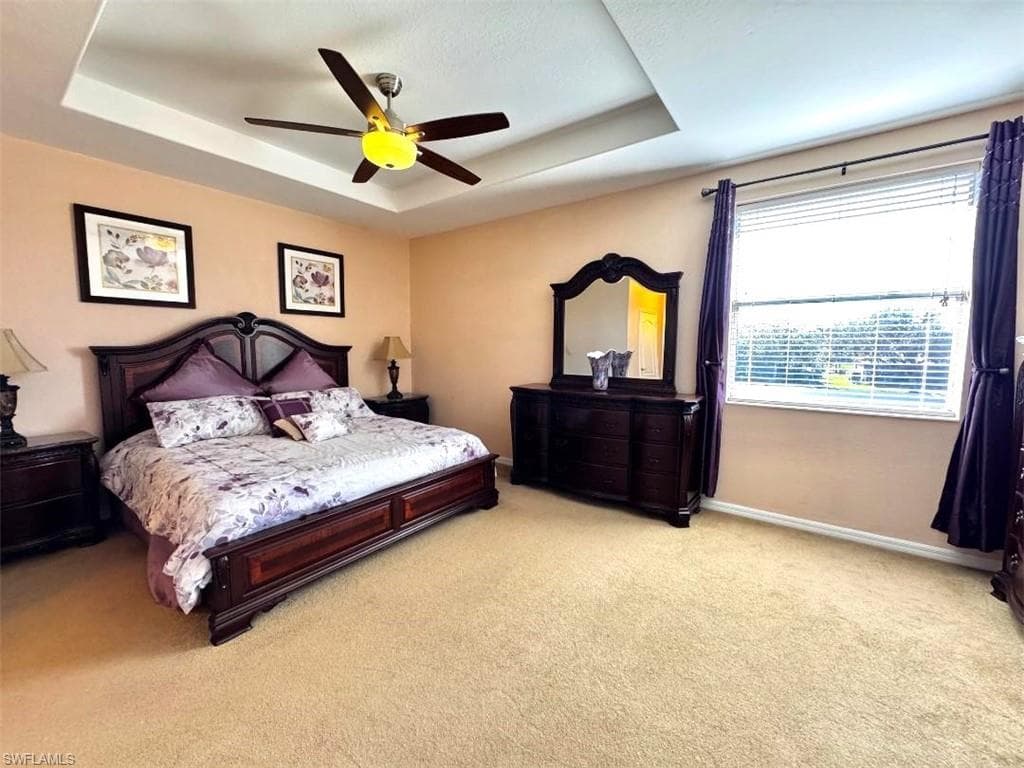 Carpeted bedroom with ceiling fan and a tray ceiling