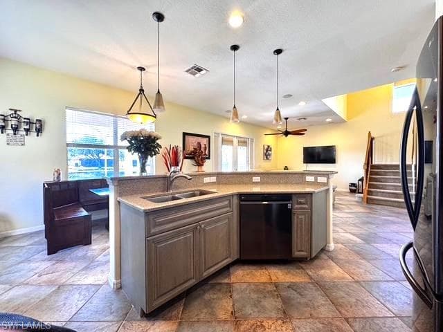 Kitchen with decorative light fixtures, an island with sink, sink, and black appliances