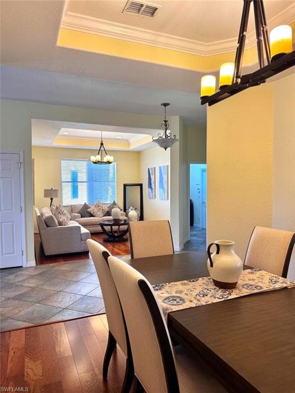 Dining room featuring crown molding, dark wood-type flooring, a chandelier, and a tray ceiling