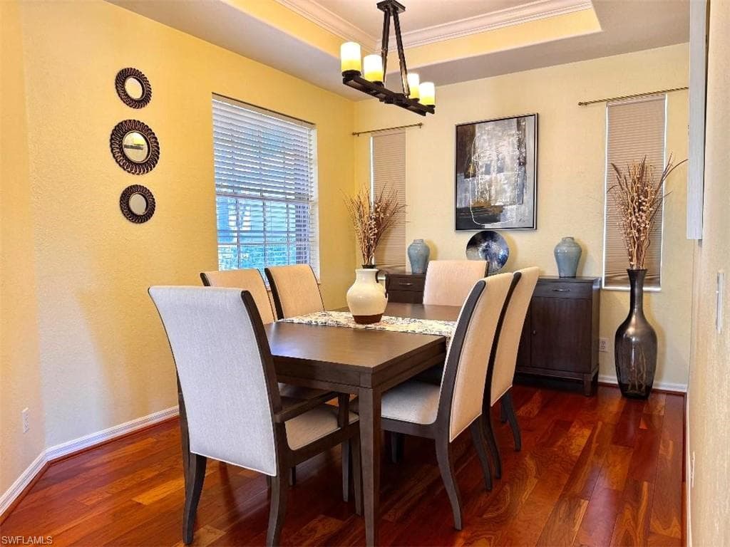 Dining space featuring crown molding, dark wood-type flooring, a raised ceiling, and a chandelier