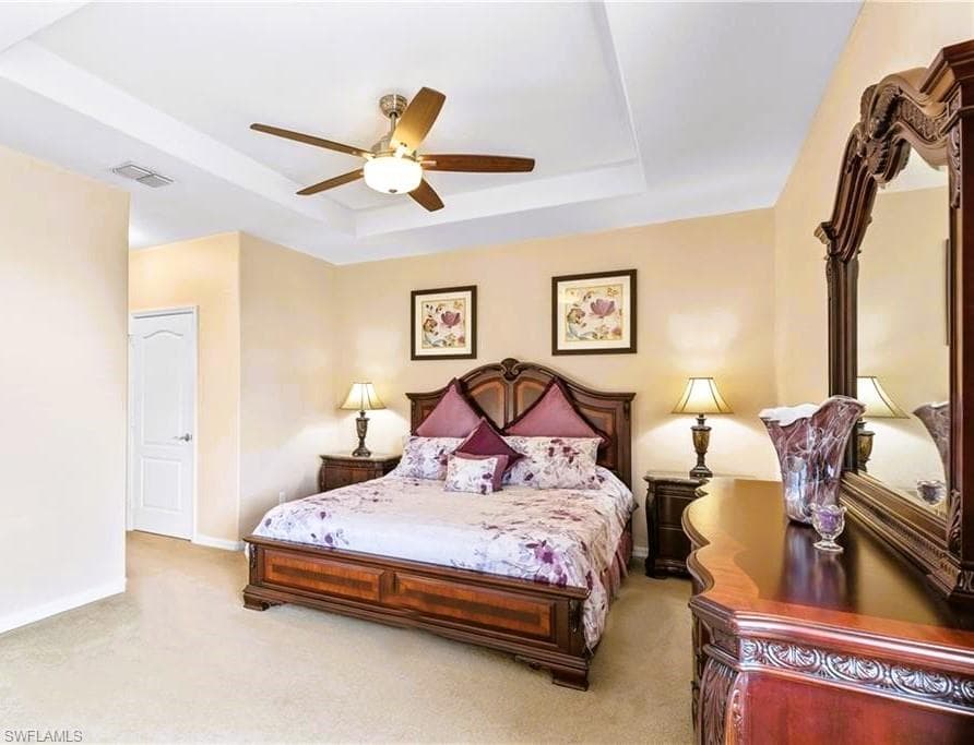 Bedroom featuring light colored carpet, ceiling fan, and a tray ceiling