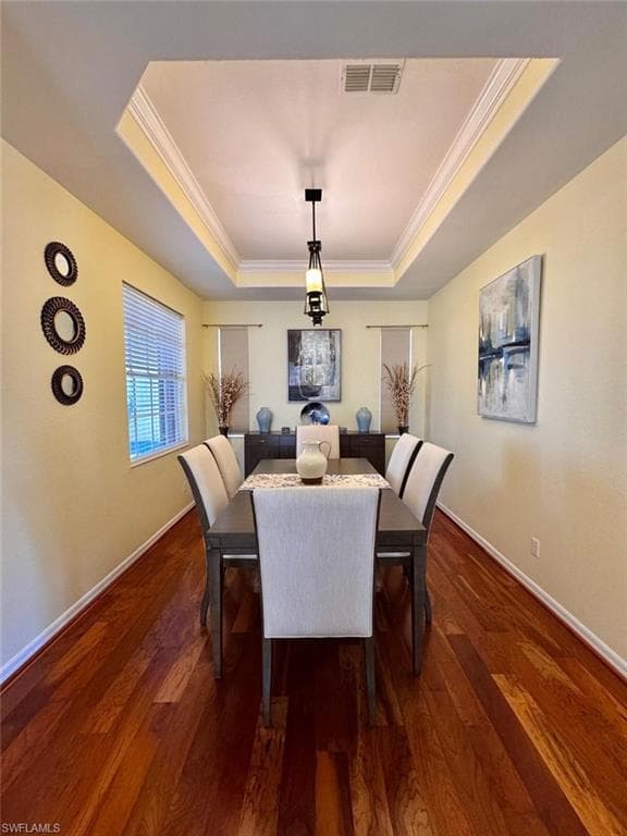 Dining room with dark wood-type flooring, a tray ceiling, and crown molding