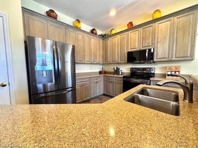 Kitchen with appliances with stainless steel finishes, light stone countertops, and sink
