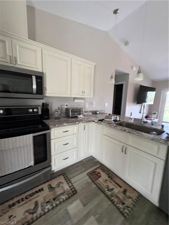 Kitchen featuring vaulted ceilings, white cabinetry, stainless steel appliances, granite-style countertops, and wood-finish flooring