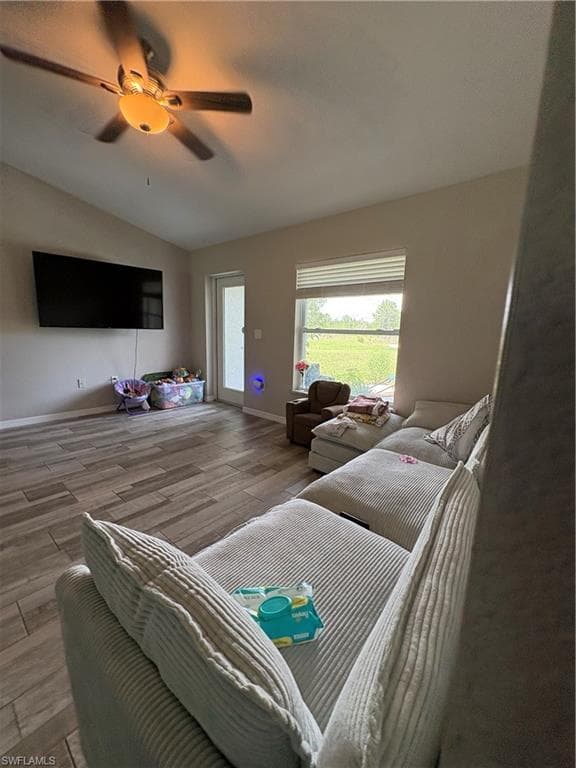 Spacious living area featuring wood-look tile flooring, a vaulted ceiling, and a ceiling fan with integrated lighting