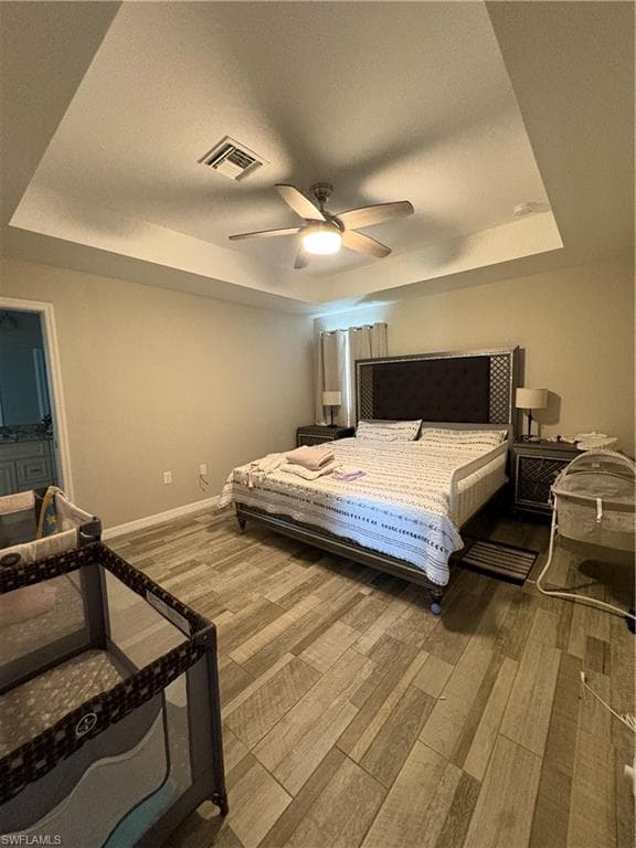 Bedroom featuring wood-finish flooring, tray ceiling, and a ceiling fan with integrated lighting