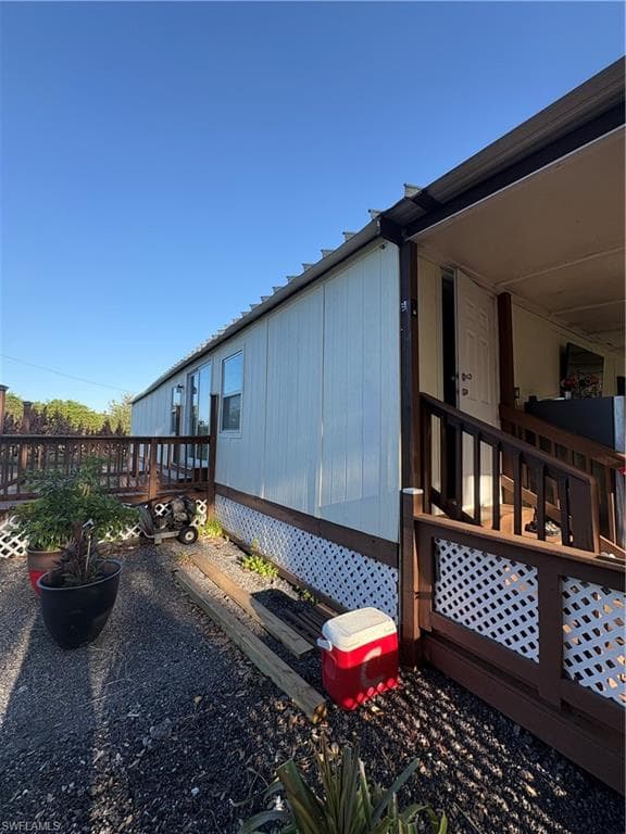 Exterior siding with white lattice foundation skirting, a covered porch with dark wood railings, and an outdoor deck