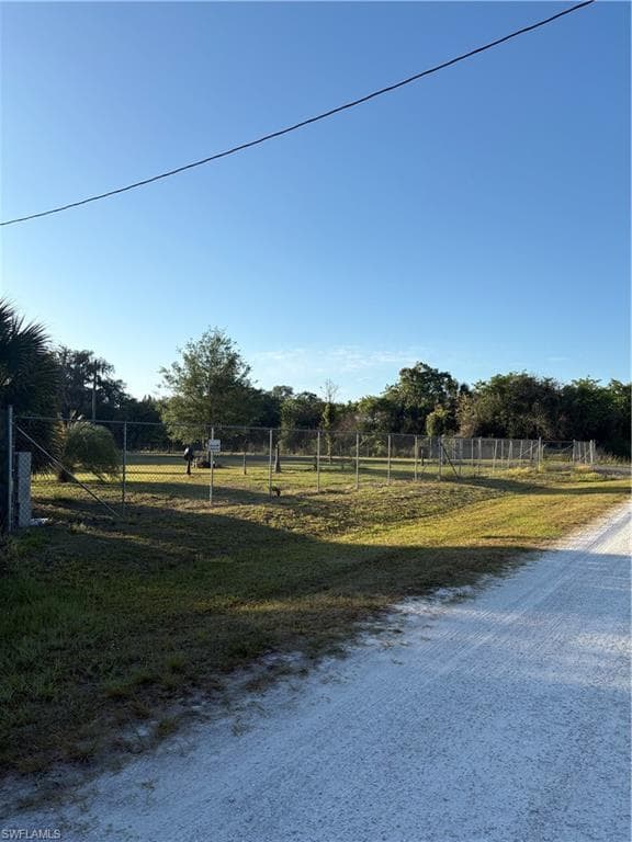 Expansive lot featuring a chain-link fence, mature trees, and a gravel road frontage