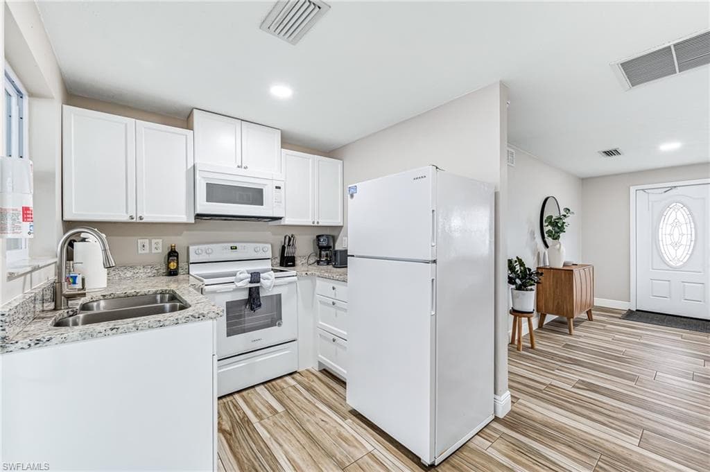 Kitchen featuring white cabinets, white appliances, light stone countertops, and sink