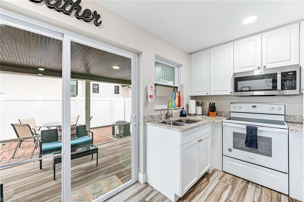Kitchen featuring electric range, light stone countertops, white cabinetry, and sink