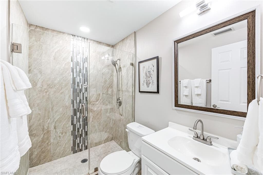 Bathroom featuring a tile shower, vanity, and toilet