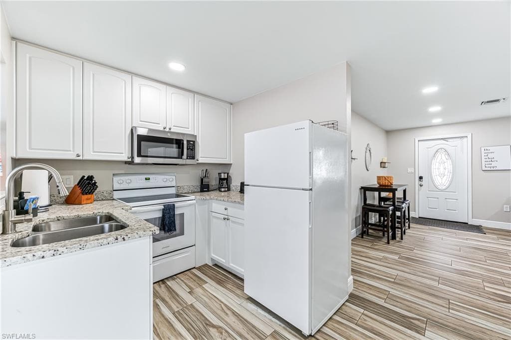 Kitchen featuring light stone counters, sink, white cabinets, and white appliances