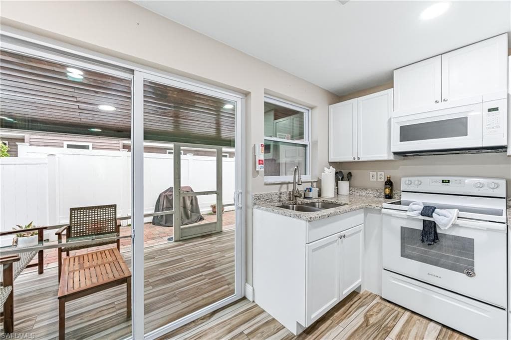 Kitchen featuring sink, white cabinets, light hardwood / wood-style floors, and white appliances