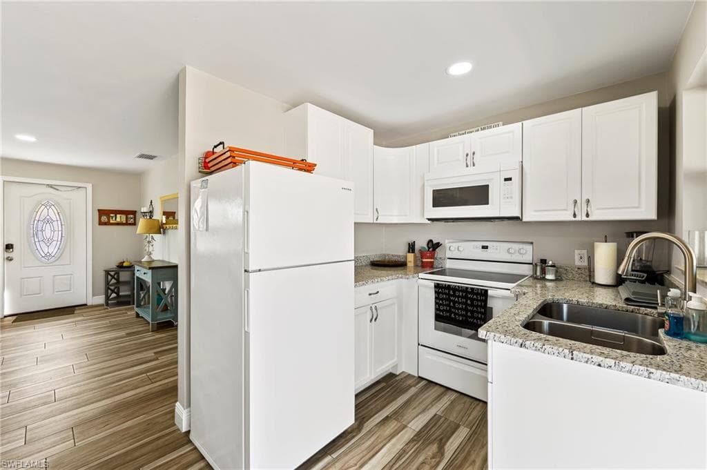 Kitchen with light stone countertops, white appliances, white cabinetry, and sink