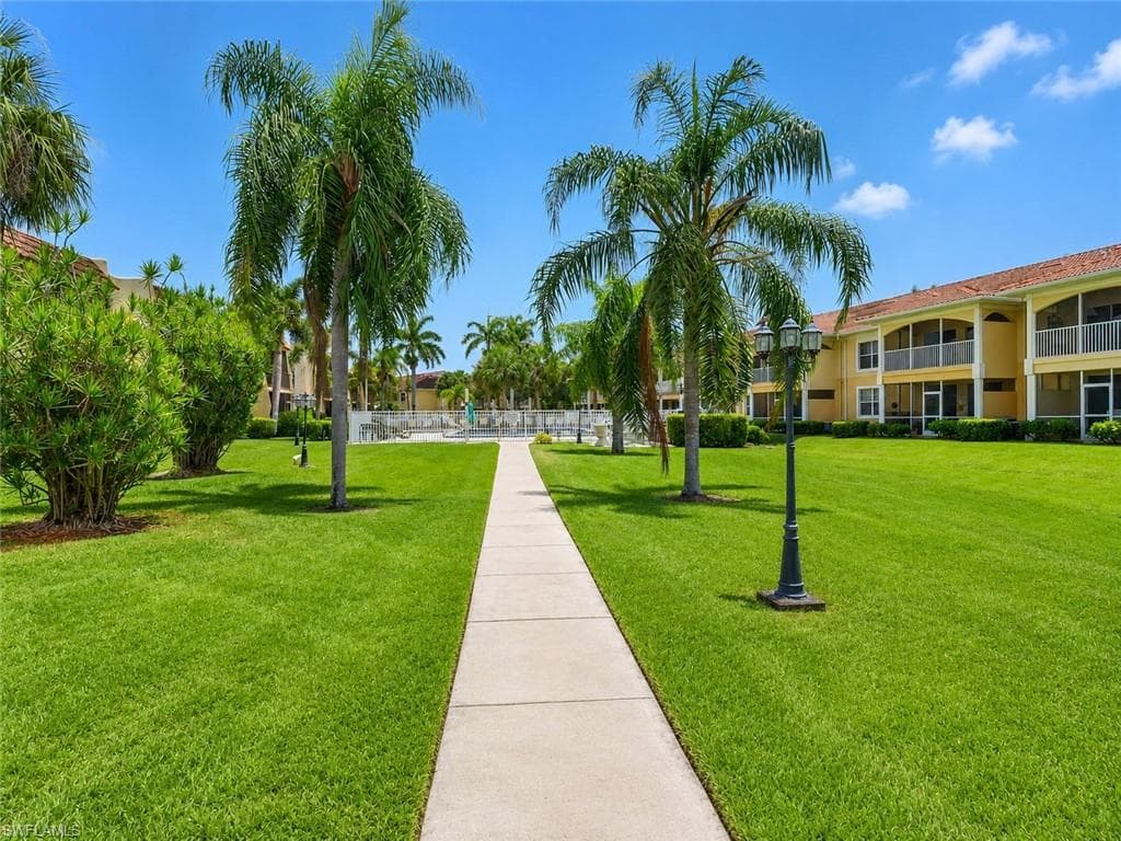 Paved walkway bordered by manicured lawns, palm trees, and established shrubbery