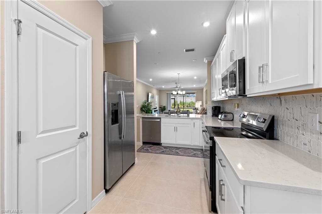 Modern kitchen featuring white cabinetry, stainless steel appliances, light-toned countertops, and a patterned tile backsplash