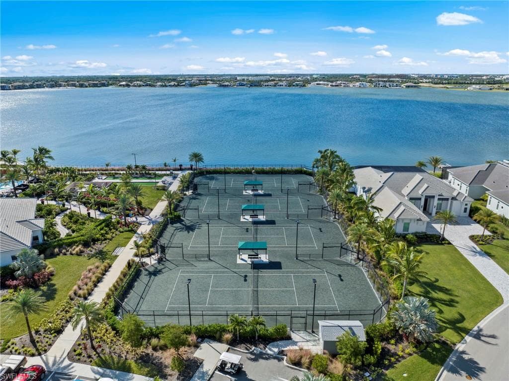 Waterfront property featuring multiple PickleBall courts, lush landscaping with palm trees, and modern residential architecture