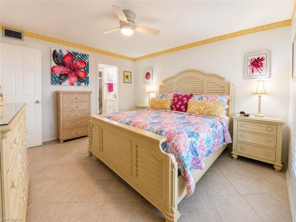 Bedroom featuring a light-colored furniture set with slatted details, neutral tile flooring, and a ceiling fan with integrated lighting