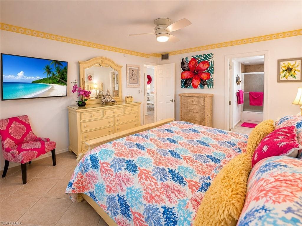 Spacious bedroom featuring neutral tile flooring, a ceiling fan with integrated lighting, and a wall-mounted television