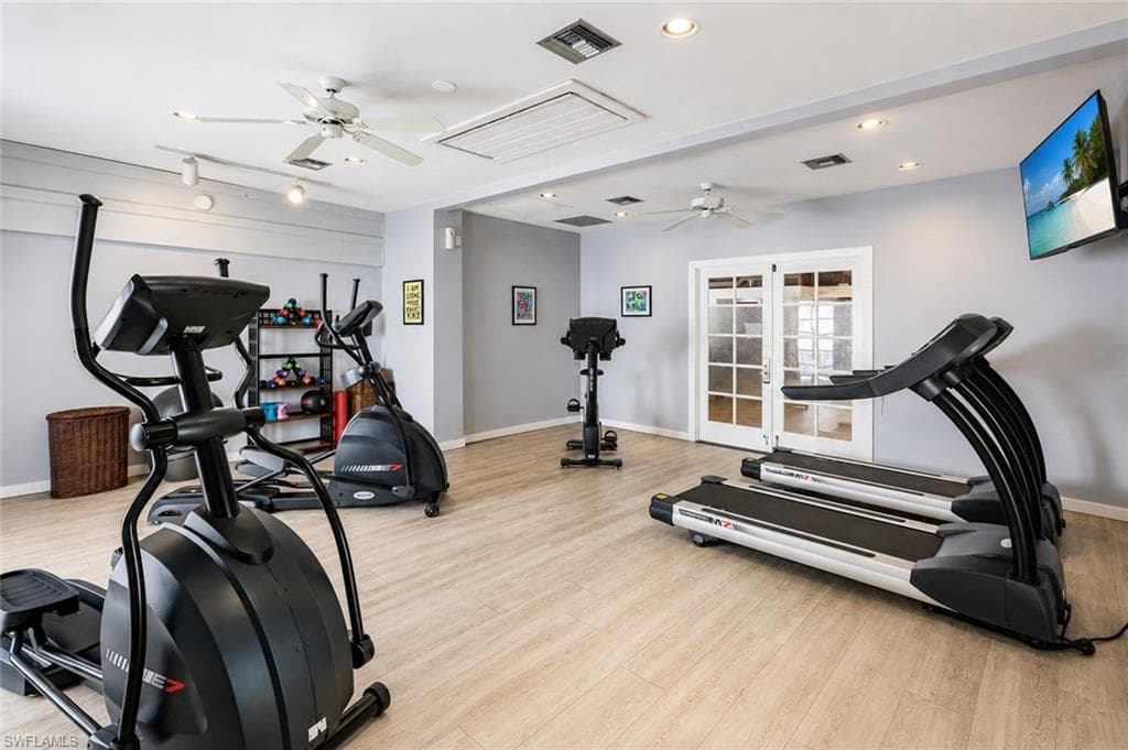 Fitness room with wood-finish flooring, two ceiling fans, recessed lighting, and double French doors with frosted glass panels