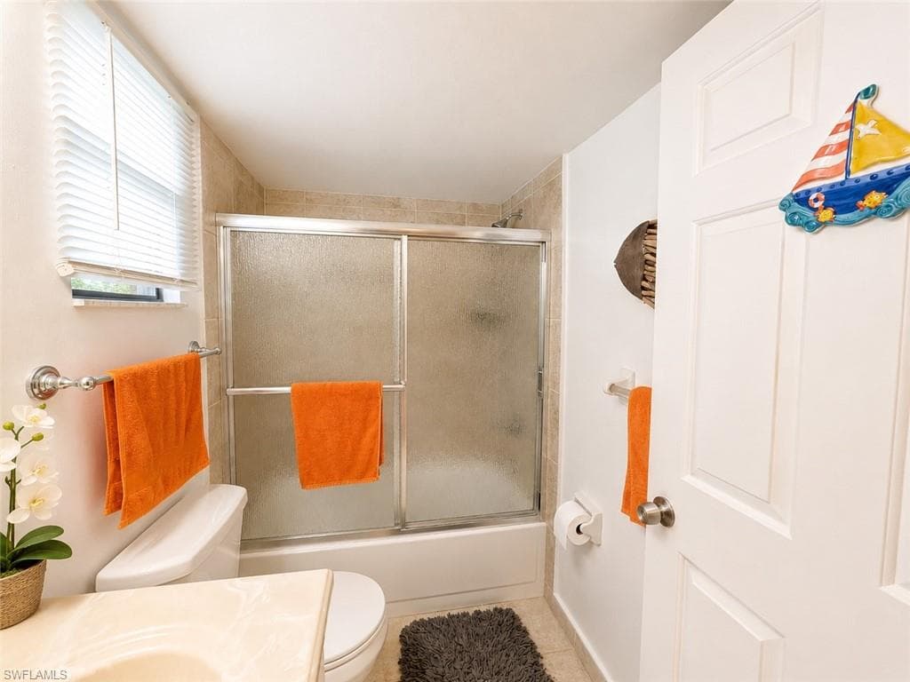 Bathroom featuring a tiled shower with sliding glass doors, a single window with horizontal blinds, and a white toilet